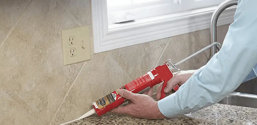 Handyman applying caulk along a kitchen backsplash and countertop seam in Lowell, MA