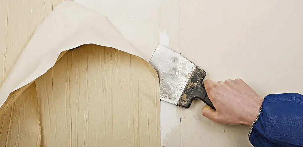 Handyman removing wallpaper with a scraper for wall preparation in Lowell, MA