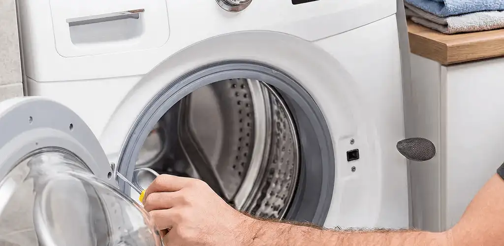 Handyman repairing a front-load washing machine and inspecting the drum in Lowell, MA